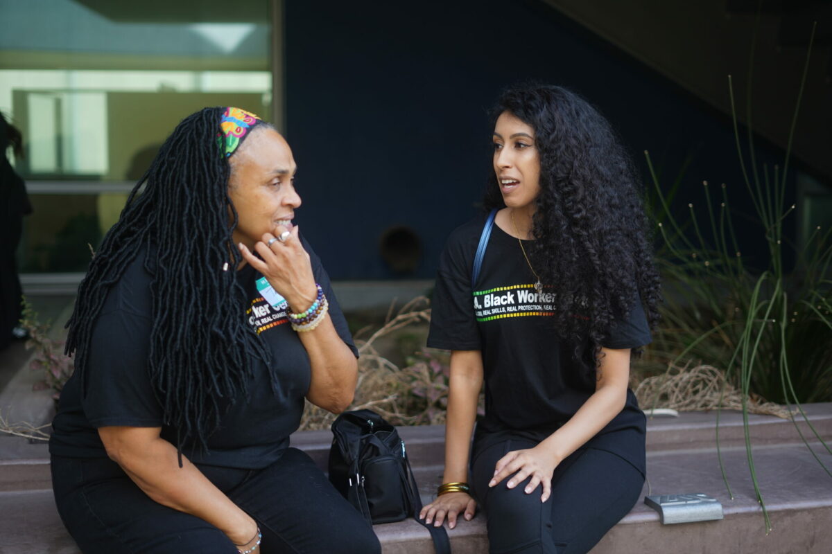 Photo of two women in black "LA Black Worker Center" T-shirts having a conversation